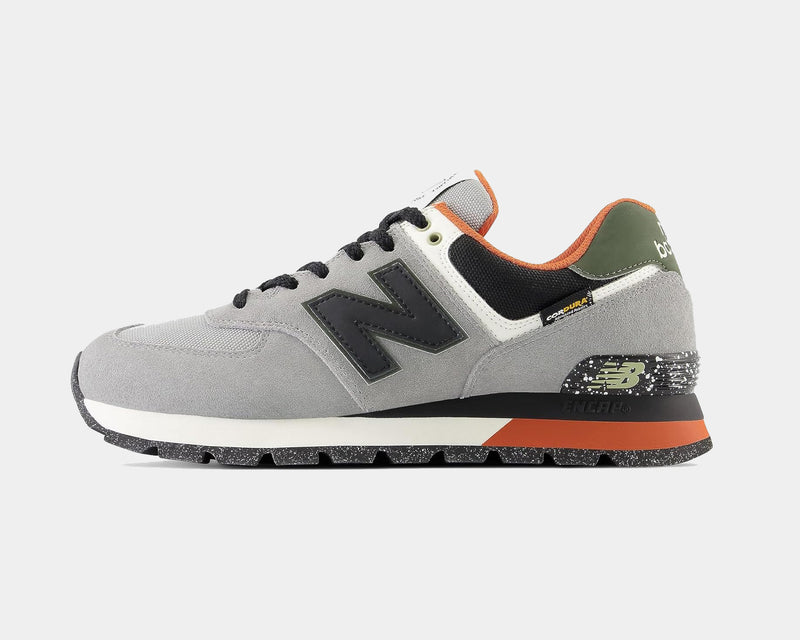 New Balance 574 Rugged sneakers in gray suede and mesh with black logo, green heel accents, and speckled outsole, side view.