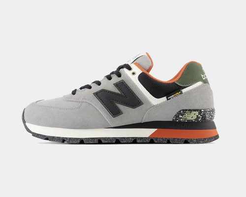New Balance 574 Rugged sneakers in gray suede and mesh with black logo, green heel accents, and speckled outsole, side view.