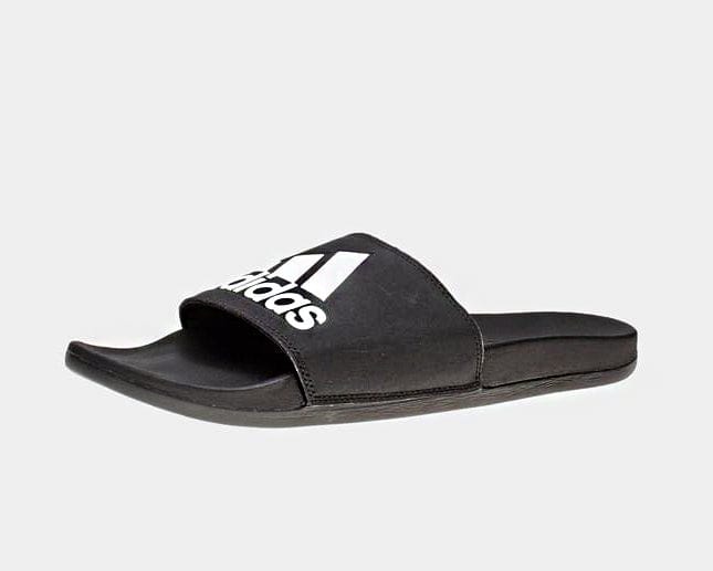 Adidas Adilette Comfort Slides in black with white Adidas logo, featuring cushioned footbed and synthetic strap, side angle view.