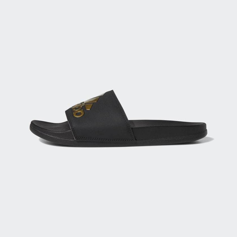 Adidas Adilette Comfort Slides in black with gold logo detailing, side view showcasing contoured footbed and slip-on design.
