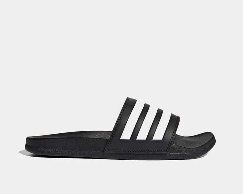 Adidas Adilette Comfort slide sandals in black with white stripes and cushioned footbed, side view.