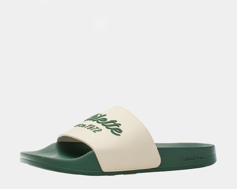 Adidas Adilette Shower Slides in beige and green with embossed text design and textured footbed, side angle view.