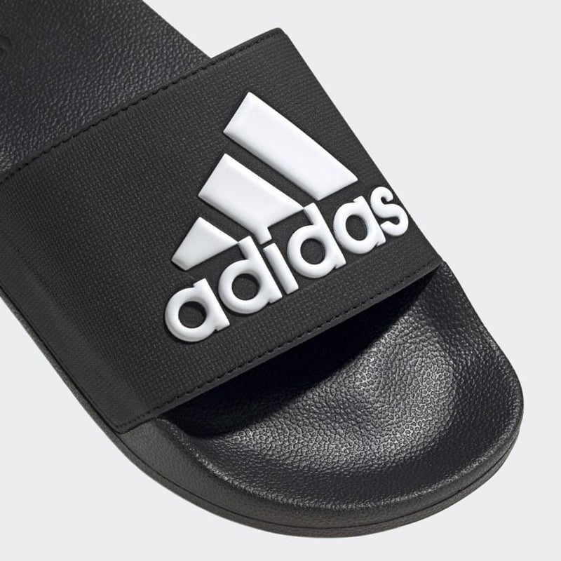 Adidas Adilette Shower Slides in black with white logo and textured footbed, close-up view of strap.