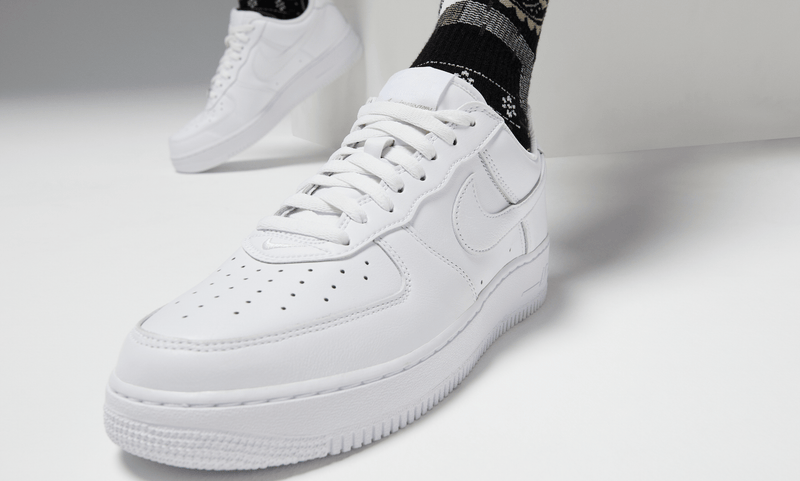 Nike Air Force 1 '07 sneakers in white leather with perforated toe box and signature Swoosh logo, angled front view worn casually.