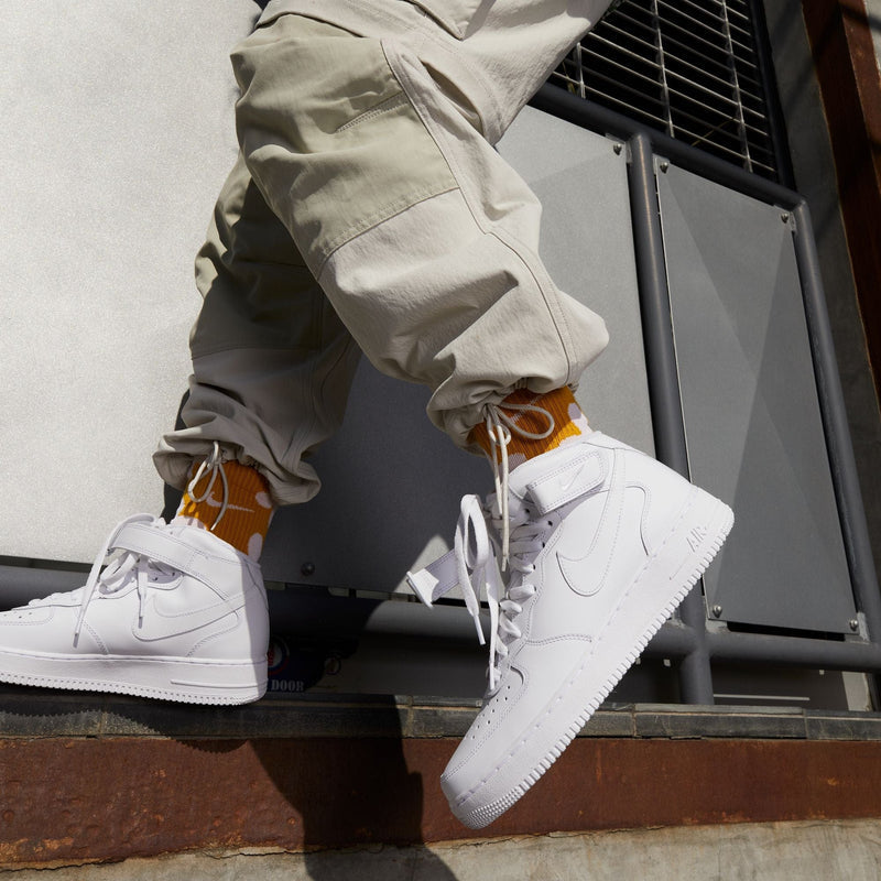 Nike Air Force 1 Mid '07 sneakers in white leather with perforated toe box and mid-top design, worn outdoors.