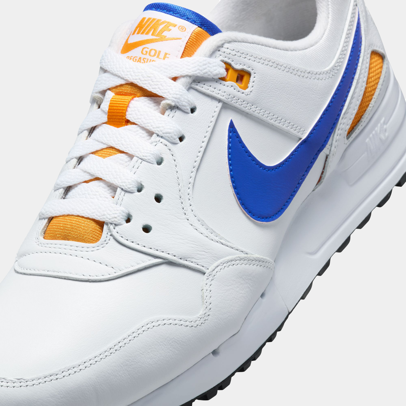Nike Air Pegasus 89' G golf shoes in white leather with blue Nike Swoosh, orange mesh accents, and white laces, angled close-up.