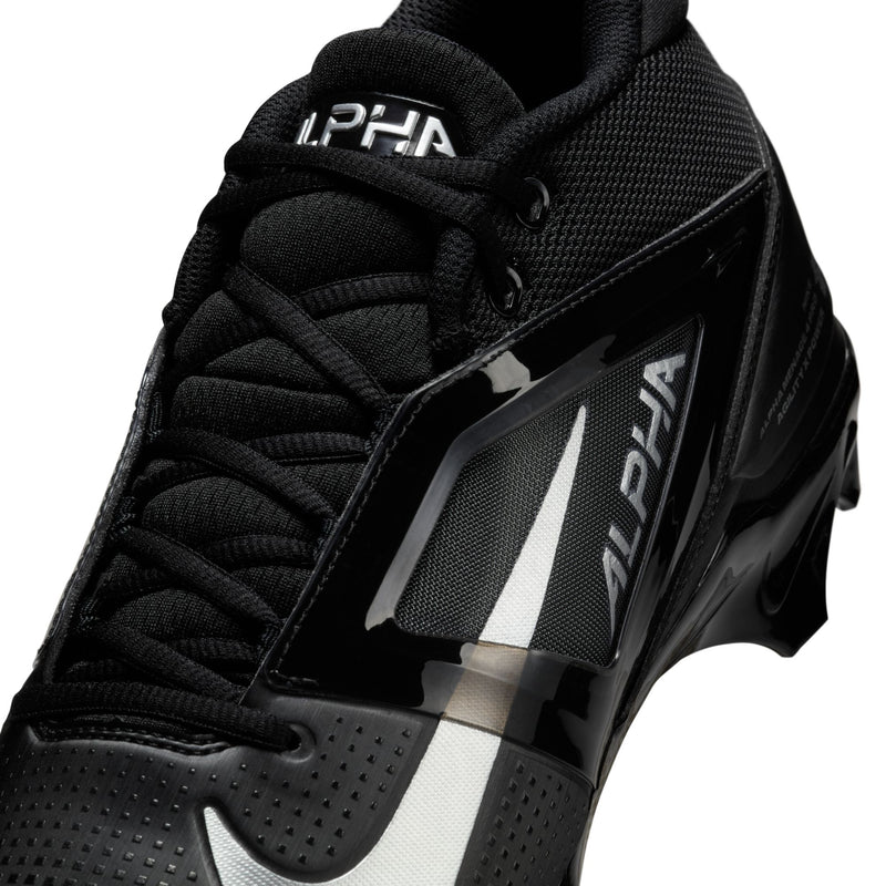 Nike Alpha Menace Elite 4 football cleats in black with mesh upper, shiny synthetic overlays, and bold "Alpha" branding, close-up perspective.