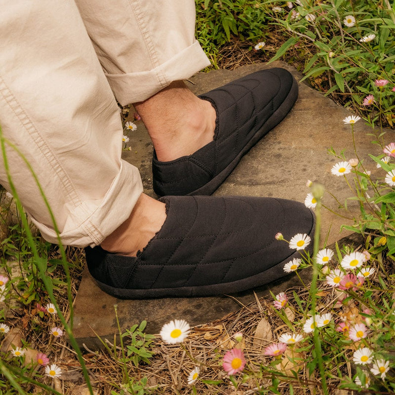SeaVees Apres Puff Slip On shoes in black with quilted puff design, worn outdoors among flowers.