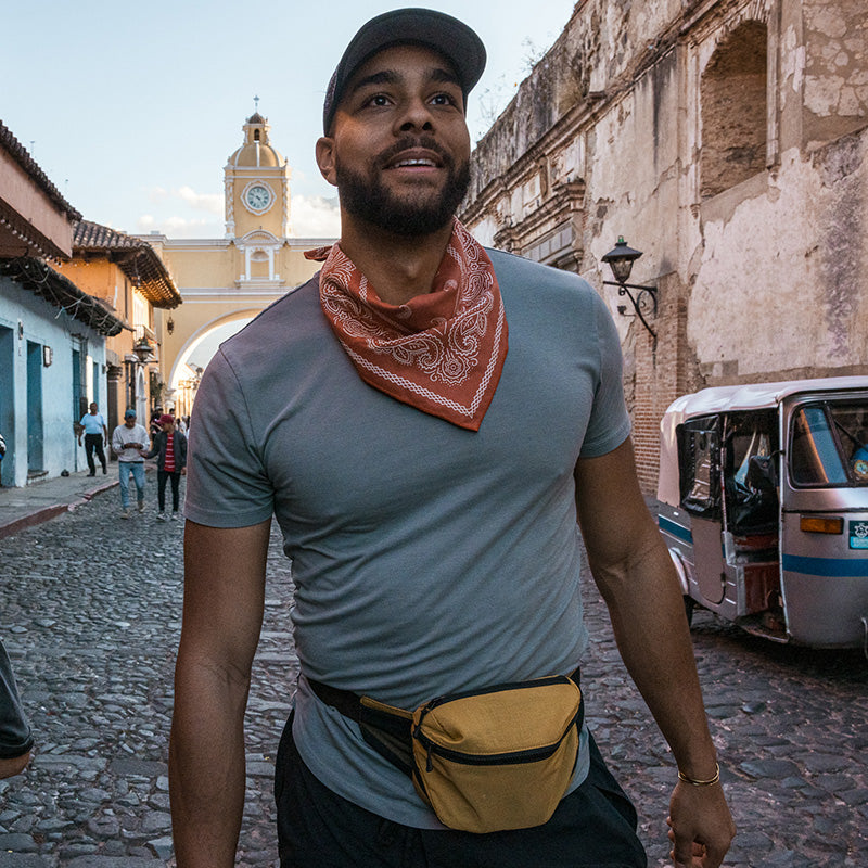 Nomadix Bandana Towel in orange with white paisley pattern, lightweight and versatile, worn around the neck during city exploration.