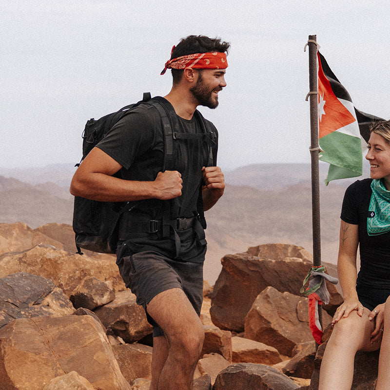 Nomadix Bandana Towel in green with a versatile design worn around the neck during an outdoor hike with desert rocks in the background.