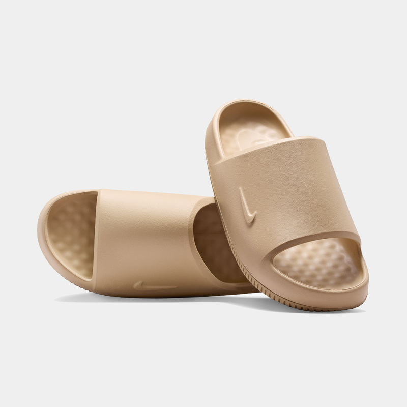 Nike Calm Slide 2.0 slides in beige with textured footbed, wide strap, and embossed Swoosh logo, angled view.
