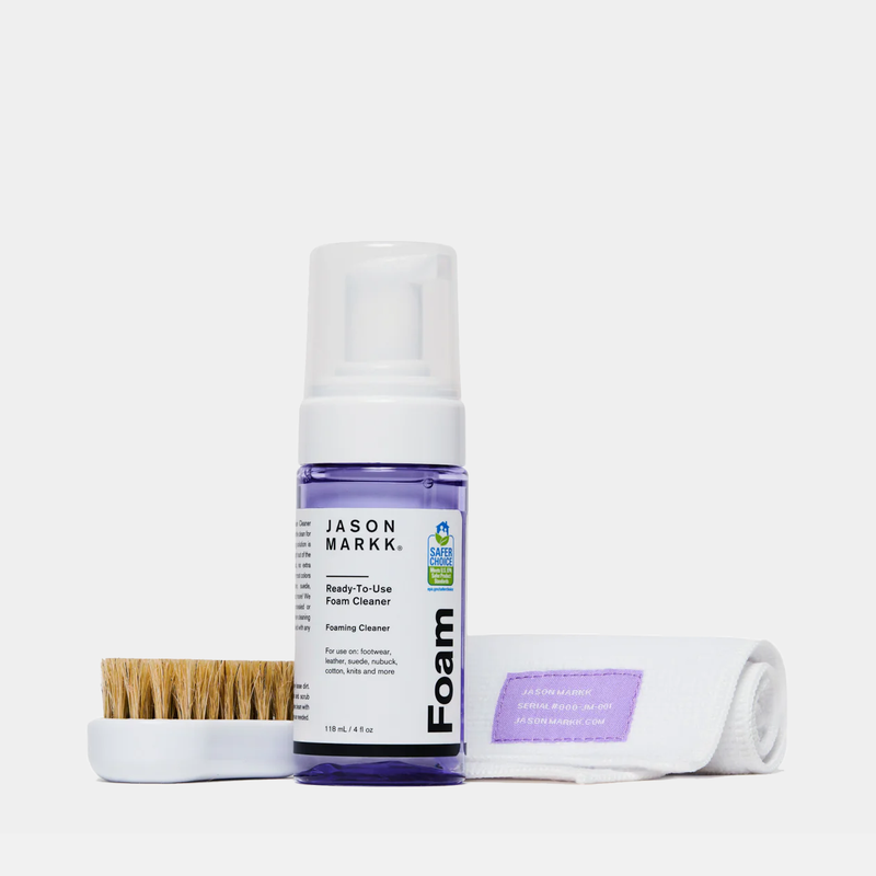 Jason Markk Complete Clean Kit featuring ready-to-use foam cleaner in a clear purple bottle, a microfiber towel, and a wooden brush with natural bristles.