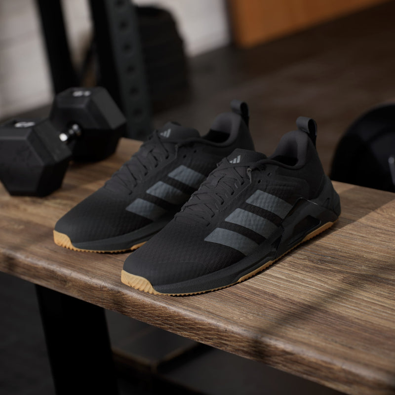Adidas Dropset Control Trainer shoes in black with gray stripes and gum sole, side angle on wooden surface.