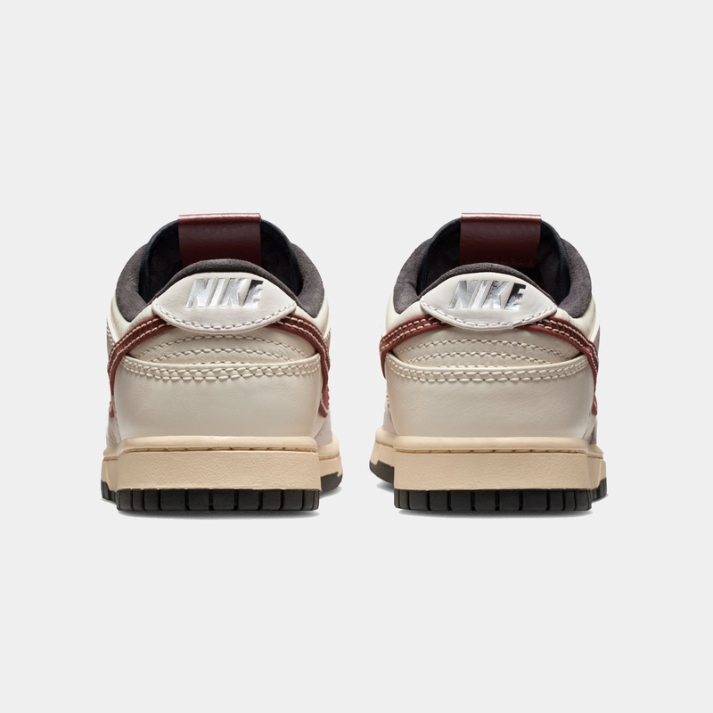 Nike Dunk Low sneakers back view showing beige leather upper with maroon accents, black outsole, and Nike branding on heel.