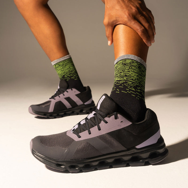 Feetures Elite Light Cushion Reflective Mini Crew socks in black with neon green reflective design and gray cuff, worn by runner.
