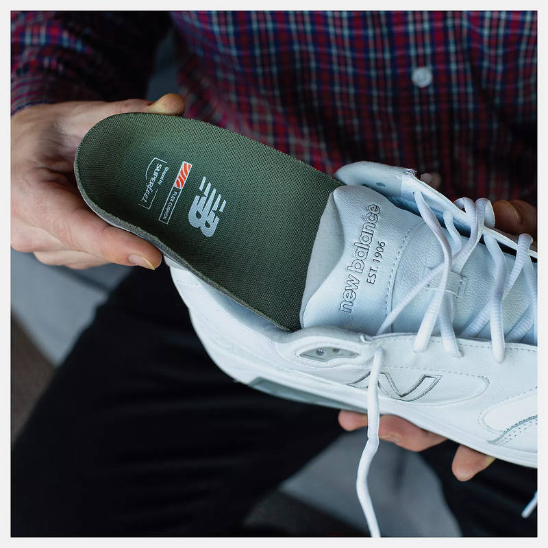 New Balance Flex Cushion Insoles in dark green with logo branding and lightweight design, shown being inserted into a white sneaker.