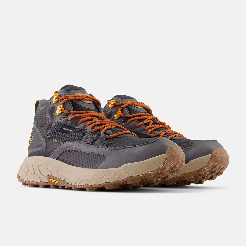 New Balance Foam X Hierro Mid GTX trail shoes in dark gray with orange laces, Vibram outsole, and Gore-Tex waterproof upper, front angle view.