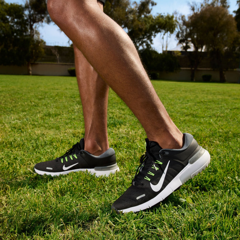 Nike Free Golf Next Nature golf shoes in black with white accents, green eyelets, and cushioned soles, worn outdoors on grass.