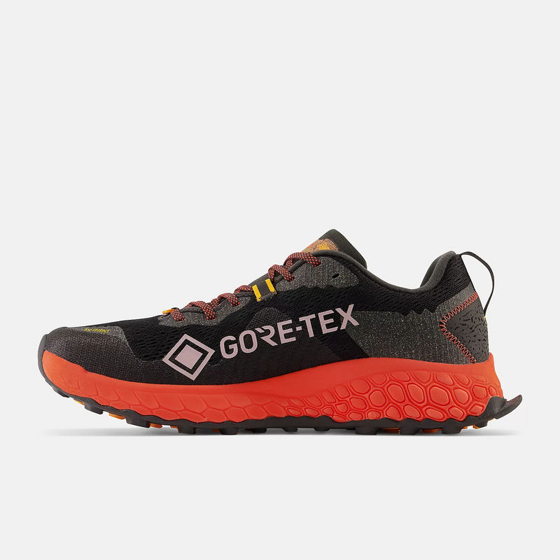 New Balance Fresh Foam Hierro v7 trail running shoes, black upper with Gore-Tex logo, orange midsole and outsole, side view.