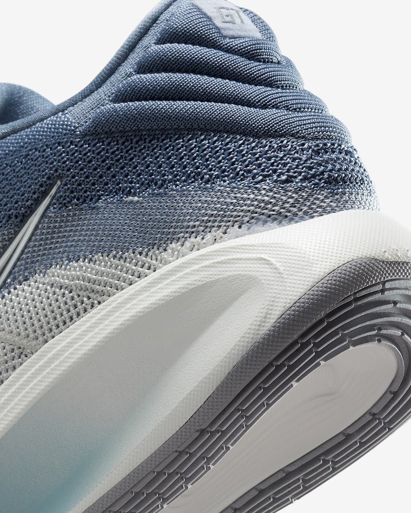 Nike G.T. Hustle 3 athletic shoes, close-up of heel area with blue woven mesh upper and textured gray and white outsole.