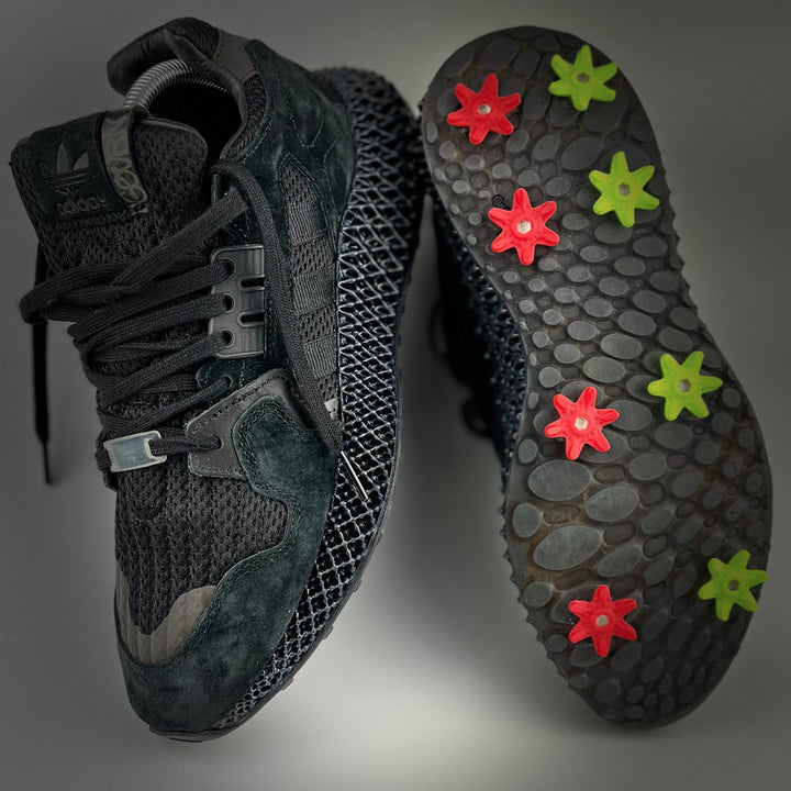 Golfkicks GOLFKICKS® V5 Traction Kit featuring red and green cleats attached to black shoe soles, bottom view.