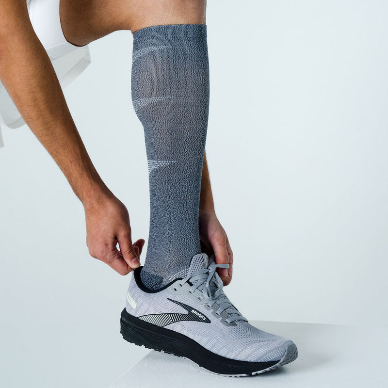 Feetures Graduated Compression Light Cushion Socks in gray with knee-high design and light cushioning, worn by man adjusting fit.