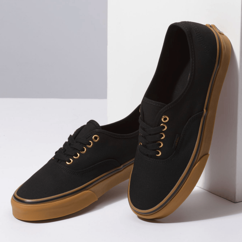 Vans Gum Authentic casual shoes in black canvas with gum sole and gold eyelets, angled front-side view.