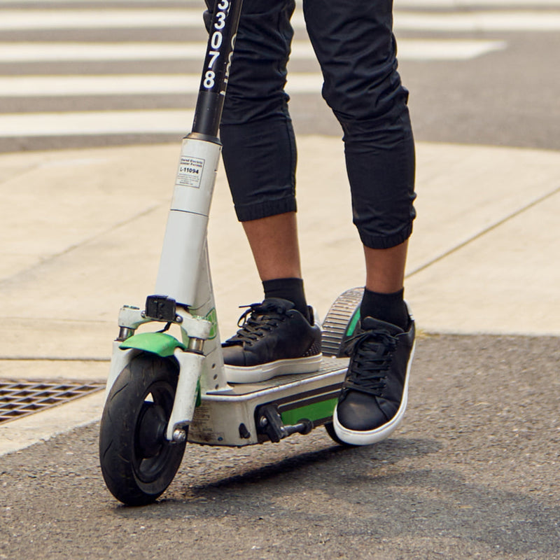 Feetures High Performance Max Cushion Quarter socks in black, offering superior comfort and cushioning, worn by a person riding a scooter.