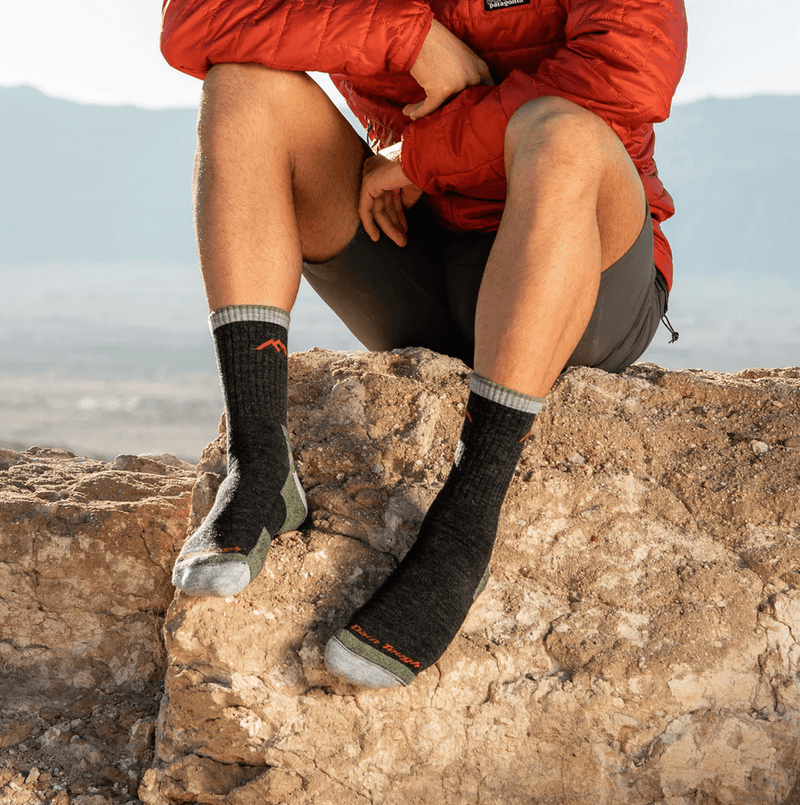 Darn Tough Hiker Micro Crew Cushion socks in black and gray with reinforced toe and heel, worn by hiker sitting outdoors.