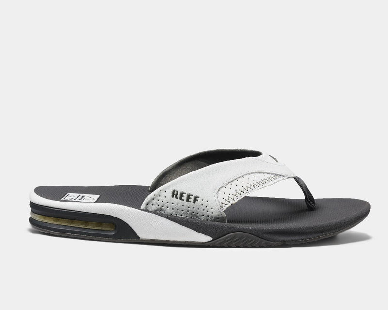 Reef Leather Fanning Flip Flops in black and white with perforated leather strap, cushioned footbed, and built-in bottle opener, side view.