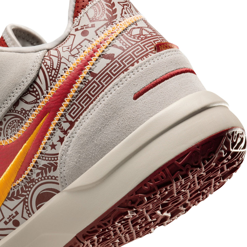 Nike LeBron NXXT Gen AMPD basketball shoes, close-up showing heel design in gray suede with red and gold accents, patterned details, and textured maroon outsole.