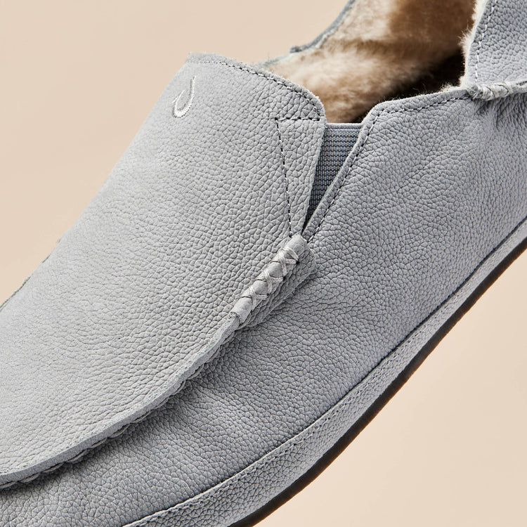 OluKai Moloa Slipper in light gray with textured leather upper, elastic side panels, and plush shearling lining, close-up view of toe box.