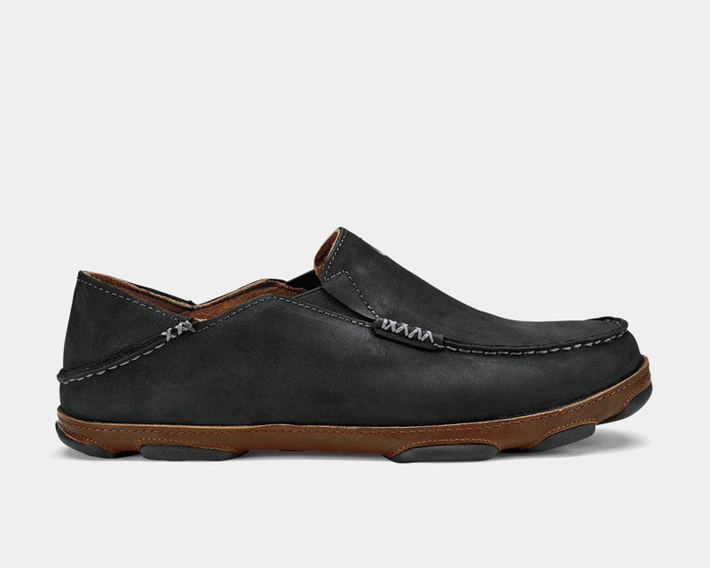 OluKai Moloa slip-on shoes in black full-grain leather with stitched detailing and brown midsole, side view.