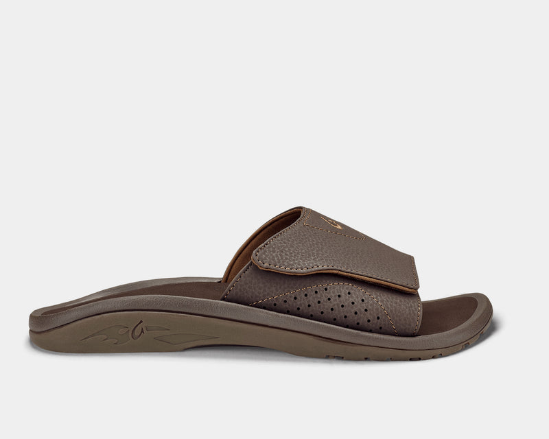 OluKai Nalu Slide sandals in dark brown with an adjustable textured strap, perforated detailing, and molded footbed, side view.