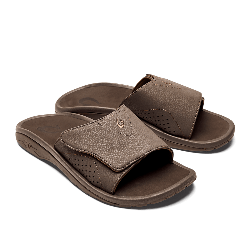 OluKai Nalu Slide sandals in brown with textured synthetic upper and perforated details, angled view showing contoured footbed.