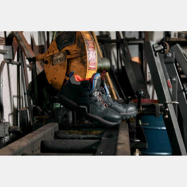 DC WorkCrew Navigator Work Hi Top Comp Toe boots in black with orange lining and blue accents, steel-toe design, industrial setting.