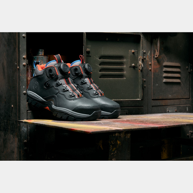 DC WorkCrew Navigator Work Hi Top Comp Toe work boots in black with red accents, durable leather upper, BOA lacing system, and rugged outsole, front angle view on industrial background.