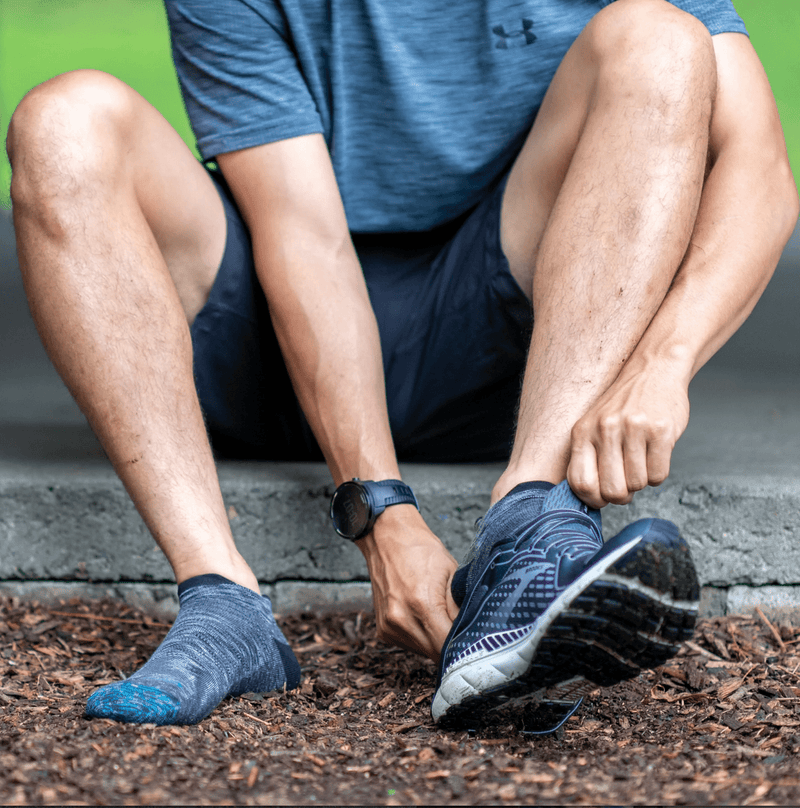 Darn Tough No Show Tab Ultra-Lightweight Running Sock in dark gray with blue accents, worn by runner adjusting shoes.