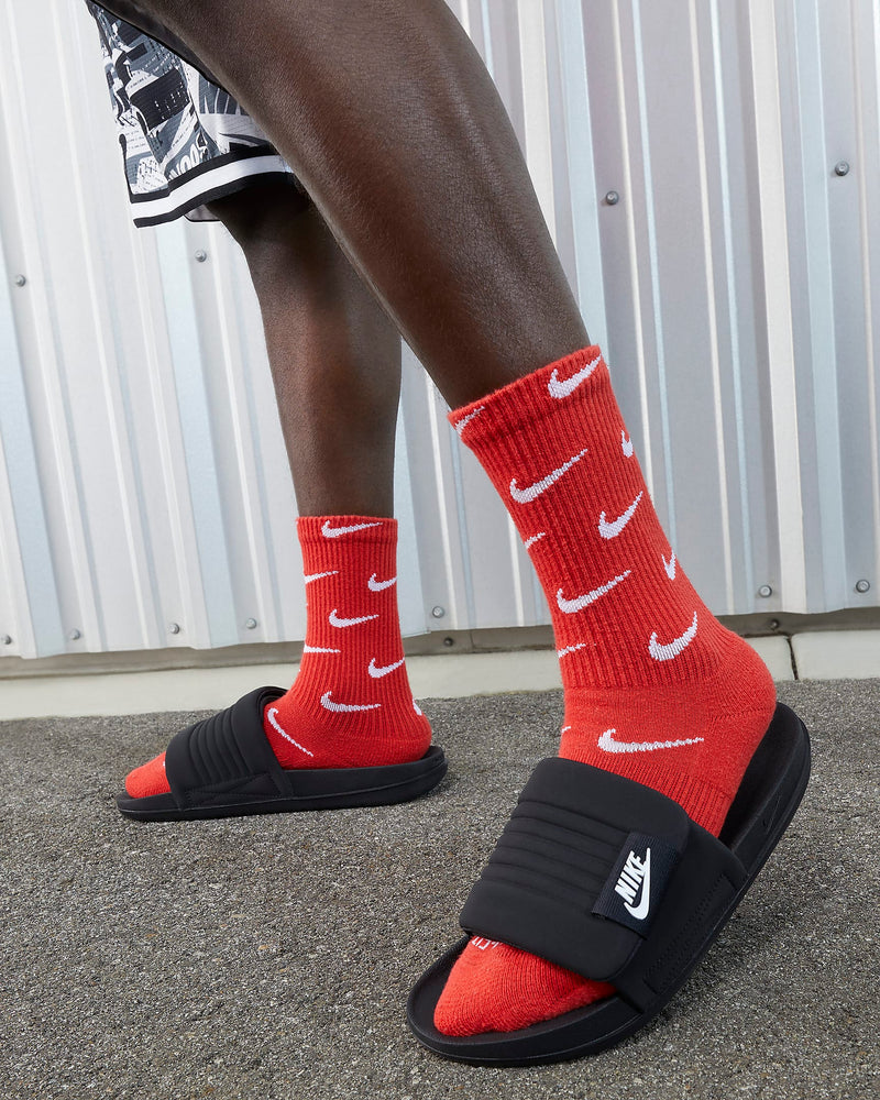 Nike Offcourt Adjustable Slide sandals in black with ribbed strap and white logo detail, worn outdoors.