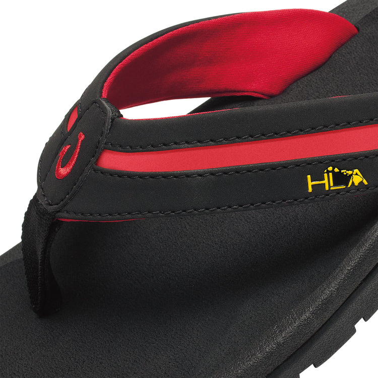 OluKai ʻOhana Pālua sandals in black and red with embroidered strap details and textured footbed, close-up side view.