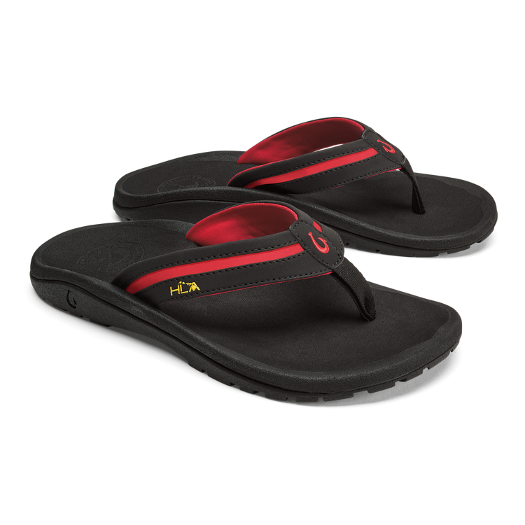 OluKai ʻOhana Pālua sandals in black with red strap accents, cushioned footbed, and durable outsole, angled view.
