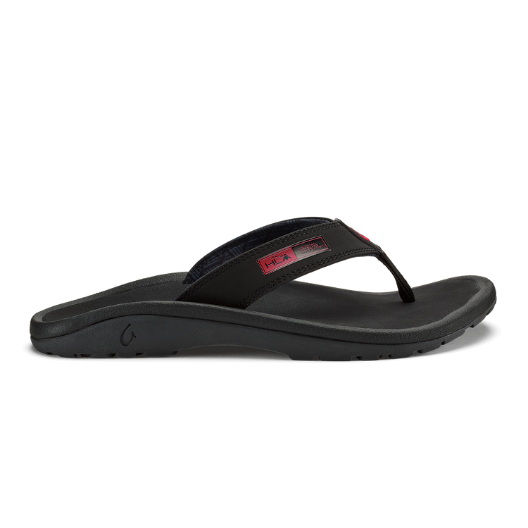 OluKai ‘Ohana sandals in black with red details, featuring a durable water-resistant strap and cushioned footbed, side view.