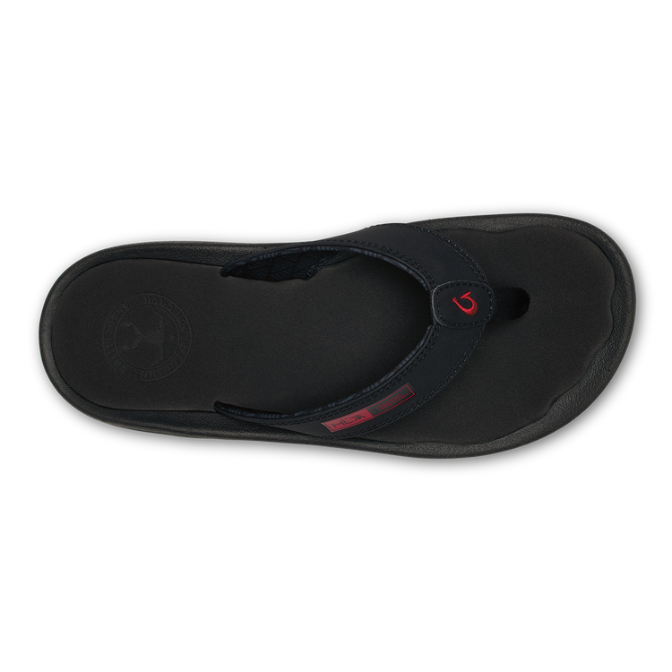 OluKai ‘Ohana sandals with black synthetic straps, red logo detail, and cushioned black footbed, top view.