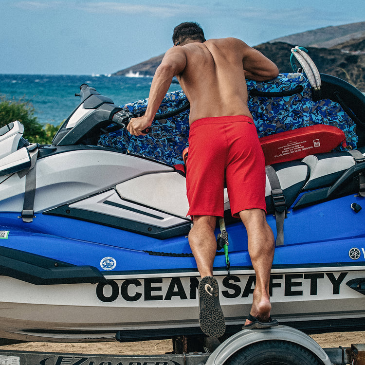 OluKai ‘Ohana flip-flops in black with textured rubber outsole and curved arch support, lifestyle view by a man on a jet ski.