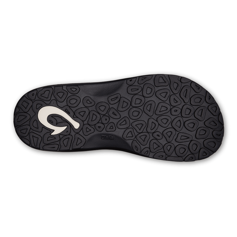 OluKai Ohana sandal outsole in black showing textured tread pattern with branding detail, sole/bottom view.