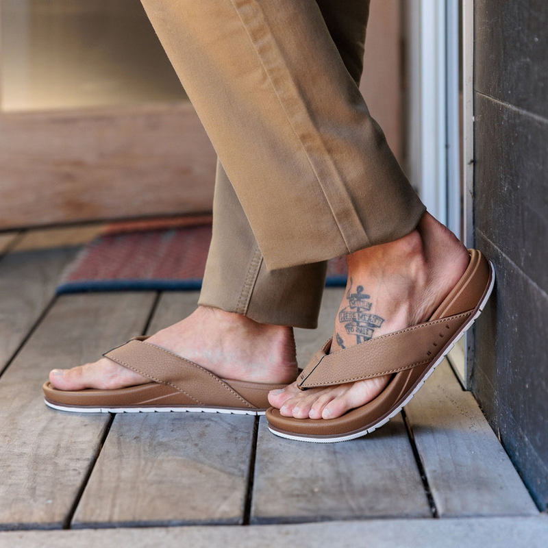Reef Phantom Bronzer sandals with brown synthetic straps and cushioned footbed, worn by person standing indoors.