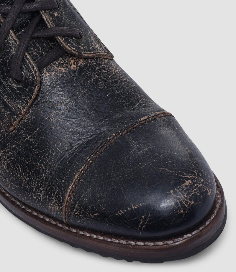 Bed Stu Protege leather shoes with distressed black finish, cap toe design, and brown welt stitching, close-up view of toe box.