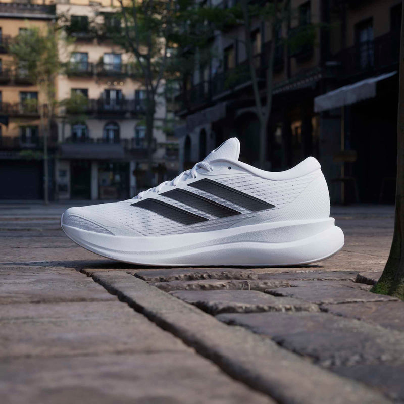 Adidas Runfalcon 6 running shoes in white with black stripes, side view on outdoor pavement.