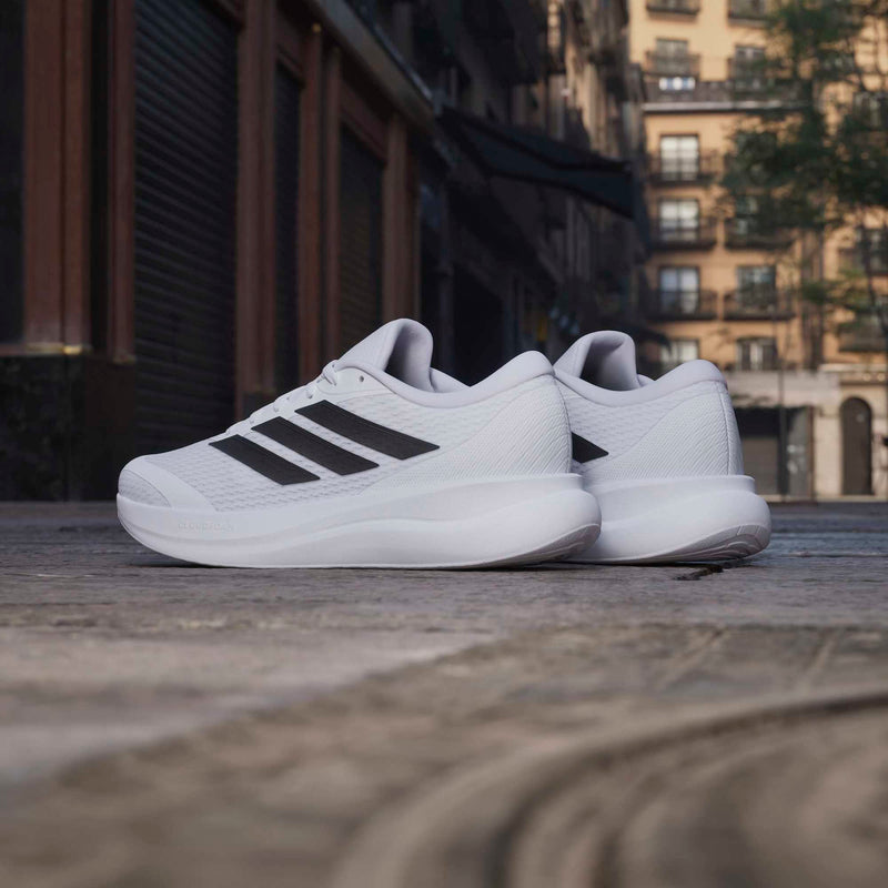 Adidas Runfalcon 6 running shoes in white with black stripes, side view on urban street background.