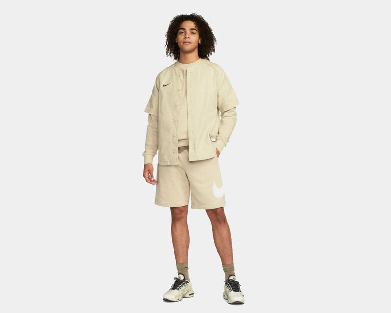 Nike Sportswear Club Shorts in beige with a white Nike logo on the left leg, worn in a casual standing pose.